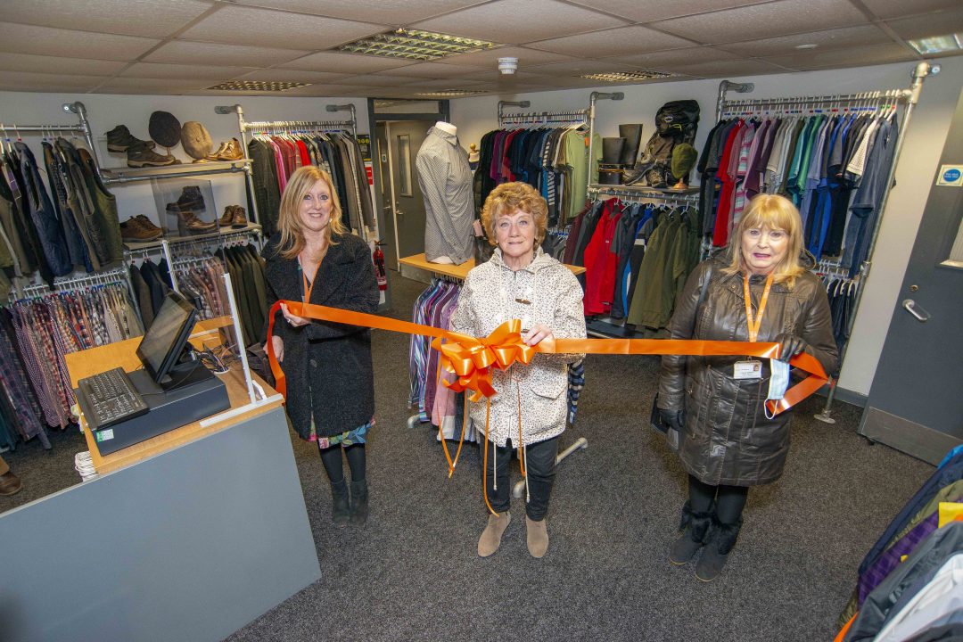 Photo of the opening of the Barnsley Hospice retail hub. Three ladies are pictured in the new clothes shop. Two of the ladies are holding an orange ribbon and the central lady is ready to cut the ribbon.