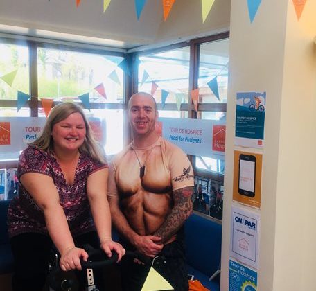 Photo of a lady sat on an exercise bike, with a man standing next to her.