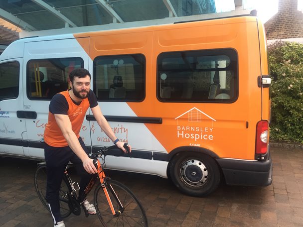 Photo of Craig Fletcher on a bicycle next to the Barnsley Hospice mini bus