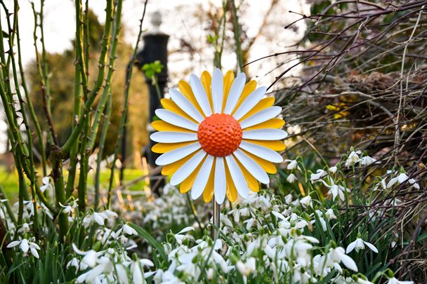 Photo of a metal daisy with yellow and white petals standing in a garden