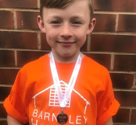 Photo of a young boy wearing a Barnsley Hospice orange coloured t-shirt and a medal on a ribbon around his neck.