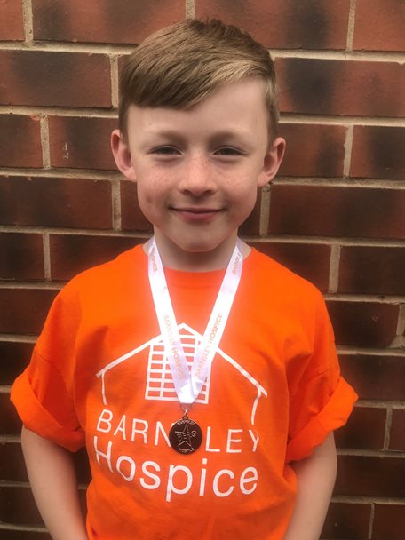 Photo of a young boy wearing a Barnsley Hospice orange coloured t-shirt and a medal on a ribbon around his neck.