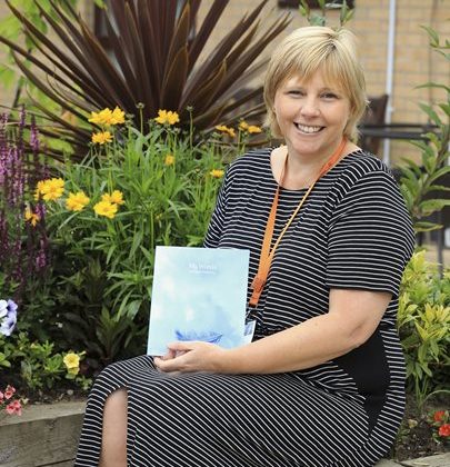 Photo of a lady seated in the Barnsley Hospice garden holding a book.