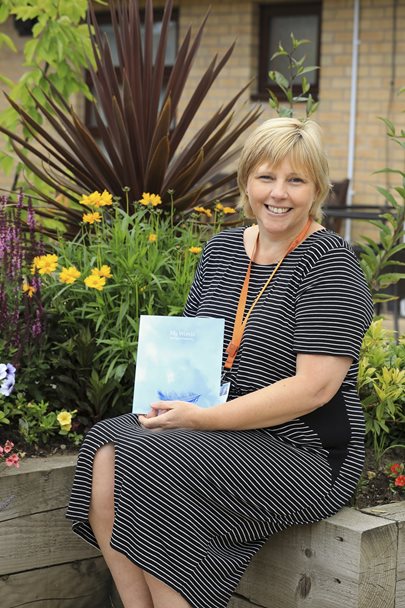 Photo of a lady seated in the Barnsley Hospice garden holding a book.