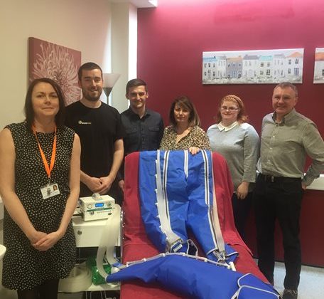 Photo of staff from Barnsley Hospice and with members of the Round Table. The group are standing around a treatment bed which has a lymphoedema garment system upon it.