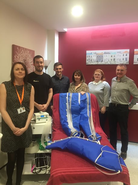 Photo of staff from Barnsley Hospice and with members of the Round Table. The group are standing around a treatment bed which has a lymphoedema garment system upon it.