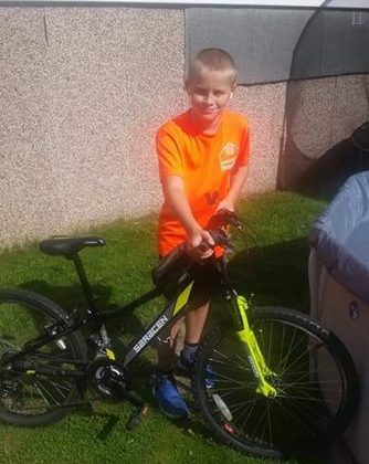 A photo of Mason Coles wearing a Barnsley Hospice t-shirt standing next to his bike
