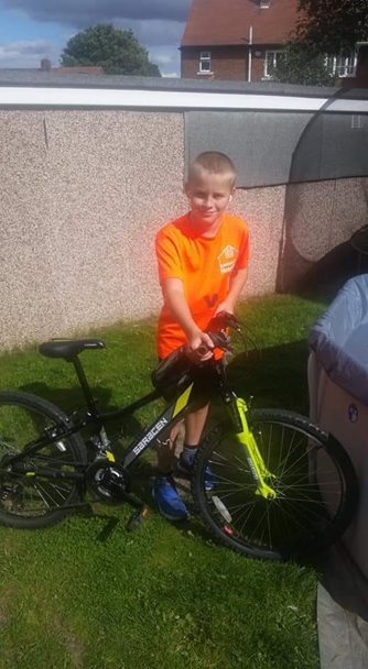 A photo of Mason Coles wearing a Barnsley Hospice t-shirt standing next to his bike