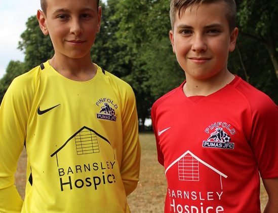 Photo of two boys wearing. One of them is wearing a red football shirt and the other a yellow shirt. The shirts have the Barnsley Hospice logo on them.