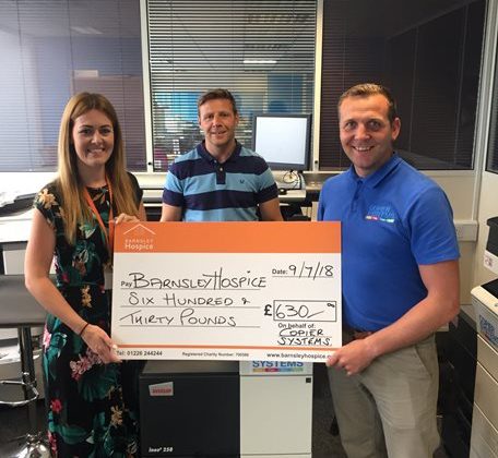 Photo of a member of the Barnsley Hospice team accepting a donation from two gentlemen from local business Copier Systems.
