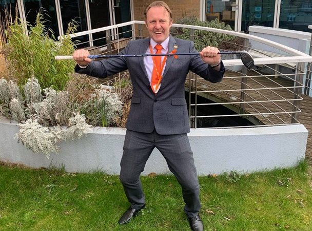 Photo of Simon Atkinson holding a golf club in the Barnsley Hospice garden