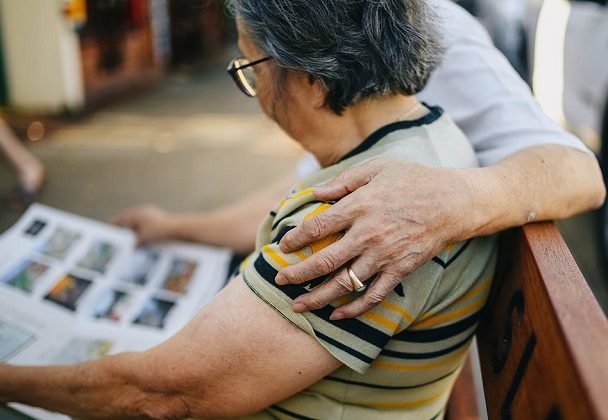 Image of two people sat on a bench, one has their arm around the other