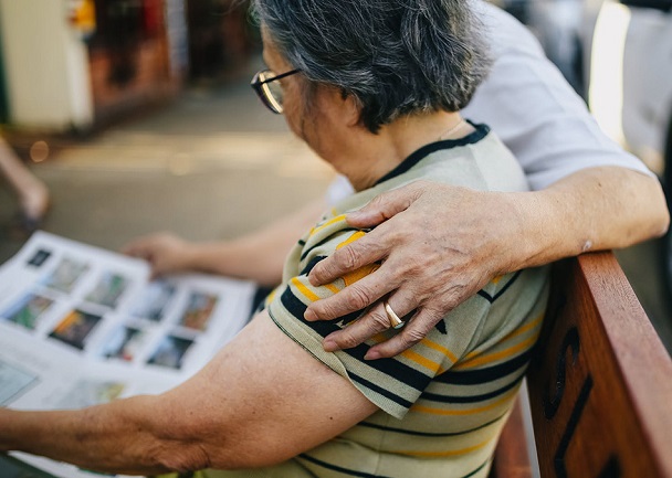 Image of two people sat on a bench, one has their arm around the other