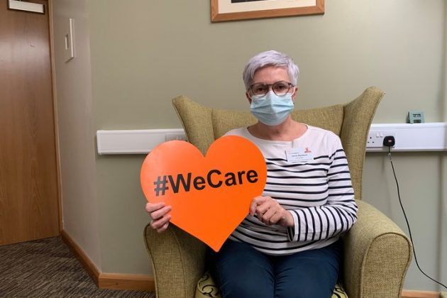 Woman sitting in armchair holding heart shaped sign #WeCare