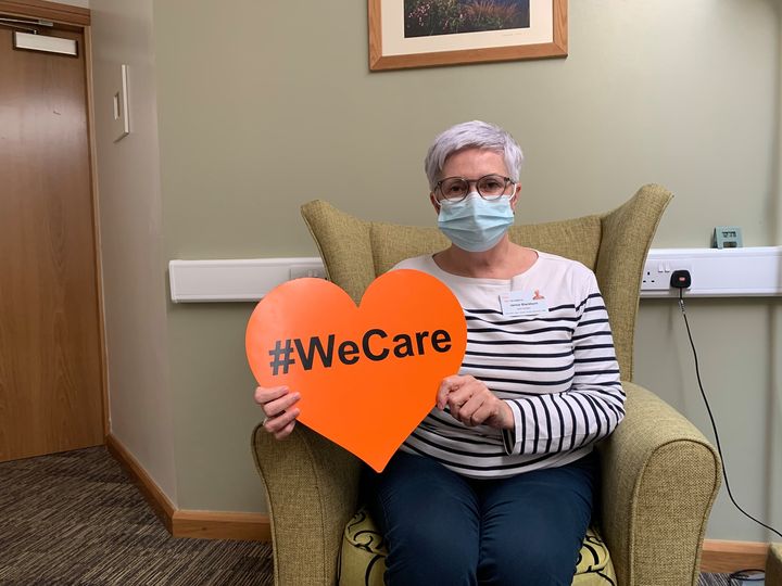 Woman sitting in armchair holding heart shaped sign #WeCare