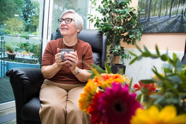 Photo of a lady seated in a comfortable leather armchair holding a cup of tea and chatting