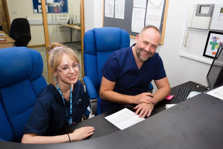 Photo of two members of the Barnsley Hospice team sat at a desk with a computer.