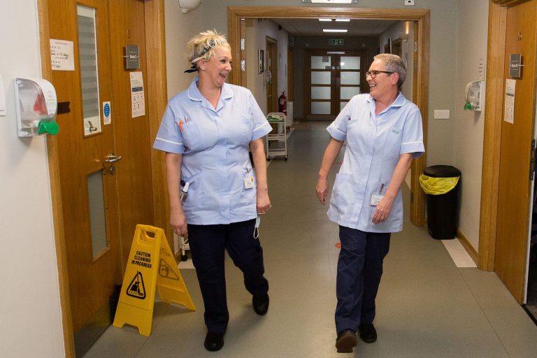 A photo of two members of the Barnsley Hospice team walking and smiling along a corridor