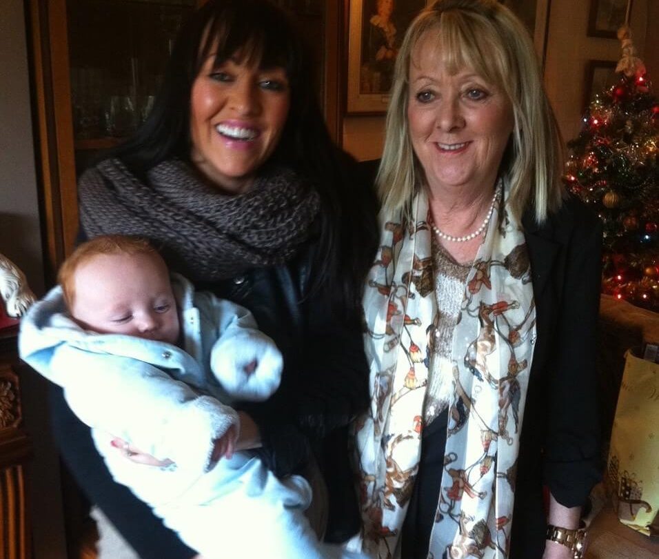Photo of Sally and Susan standing together holding a baby
