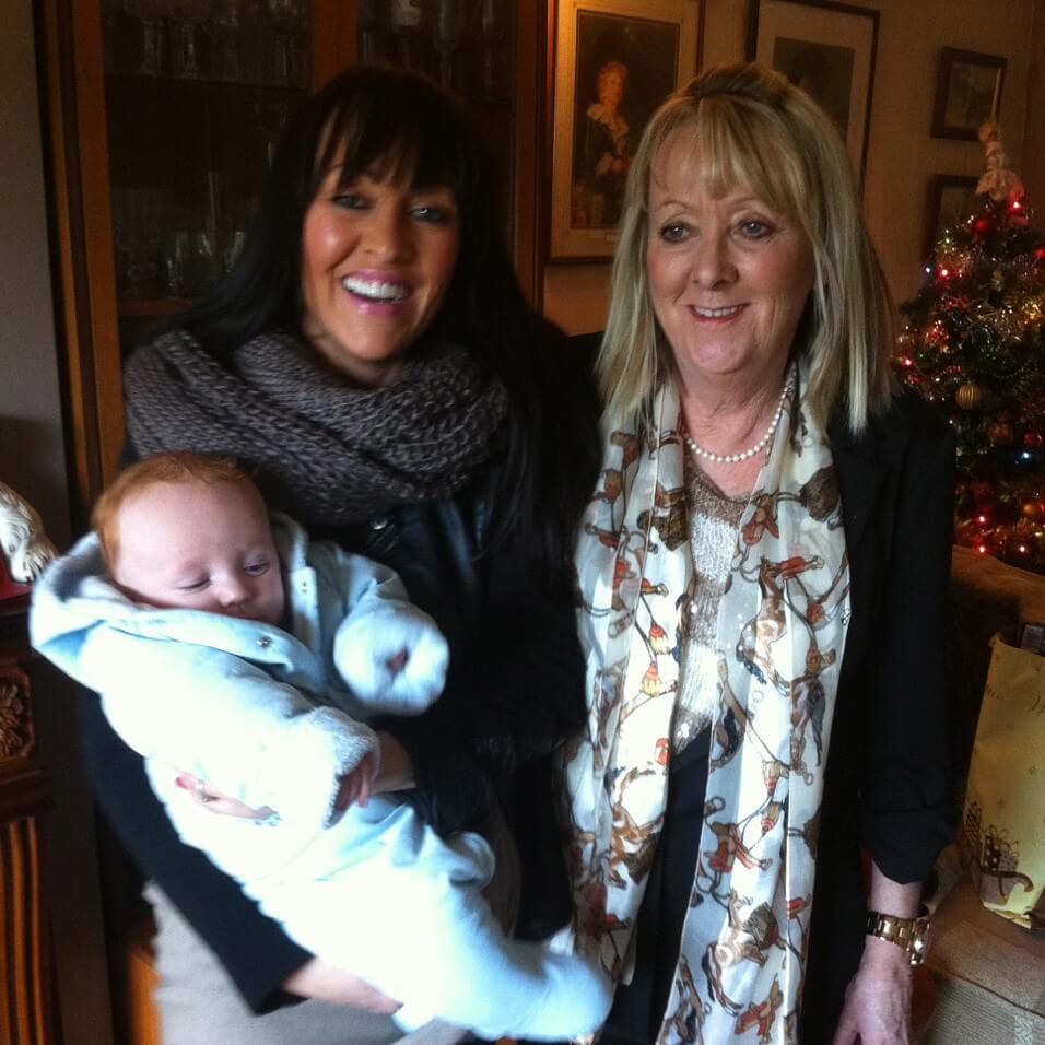 Photo of Sally and Susan standing together holding a baby