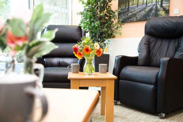 Photo of a comfortable seating area comprising of two leather armchairs and a coffee table with flowers in a vase on it.