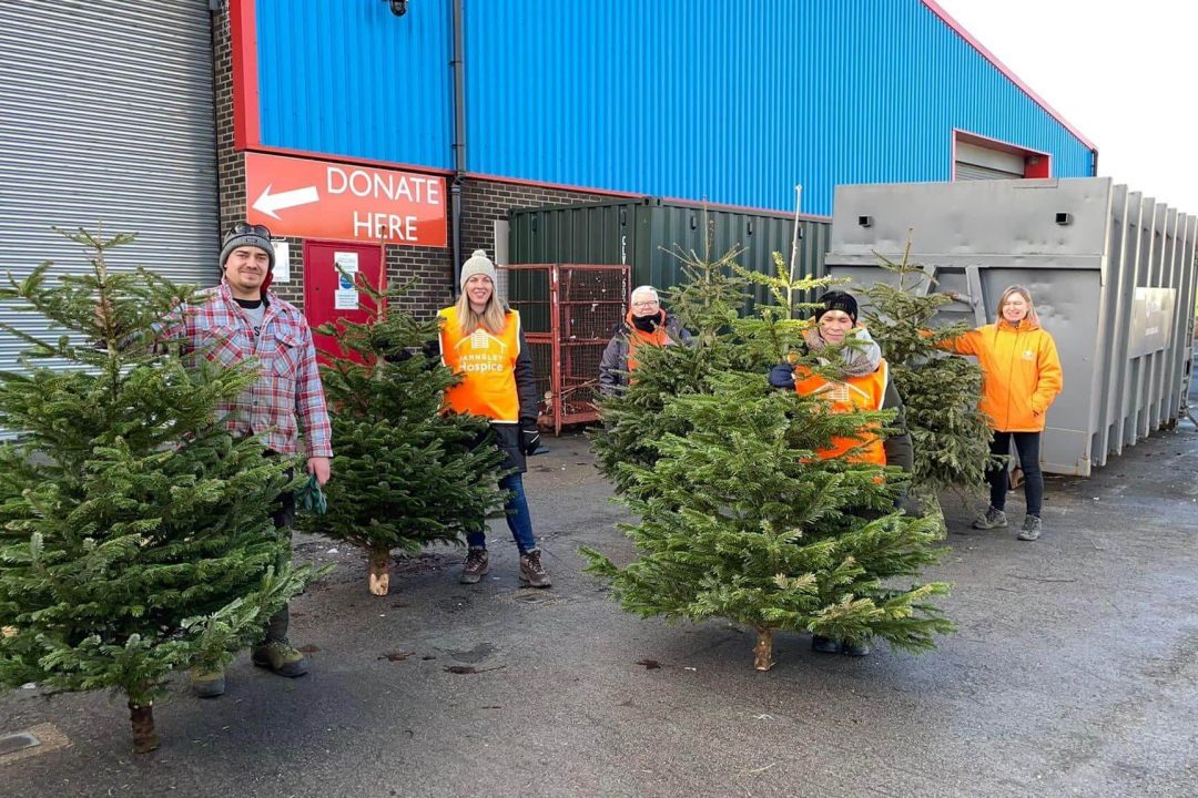 Photo of five members of the Barnsley Hospice team standing in front of the donations warehouse. They are holding Christmas trees as they assist with the Treecycle fund raising event