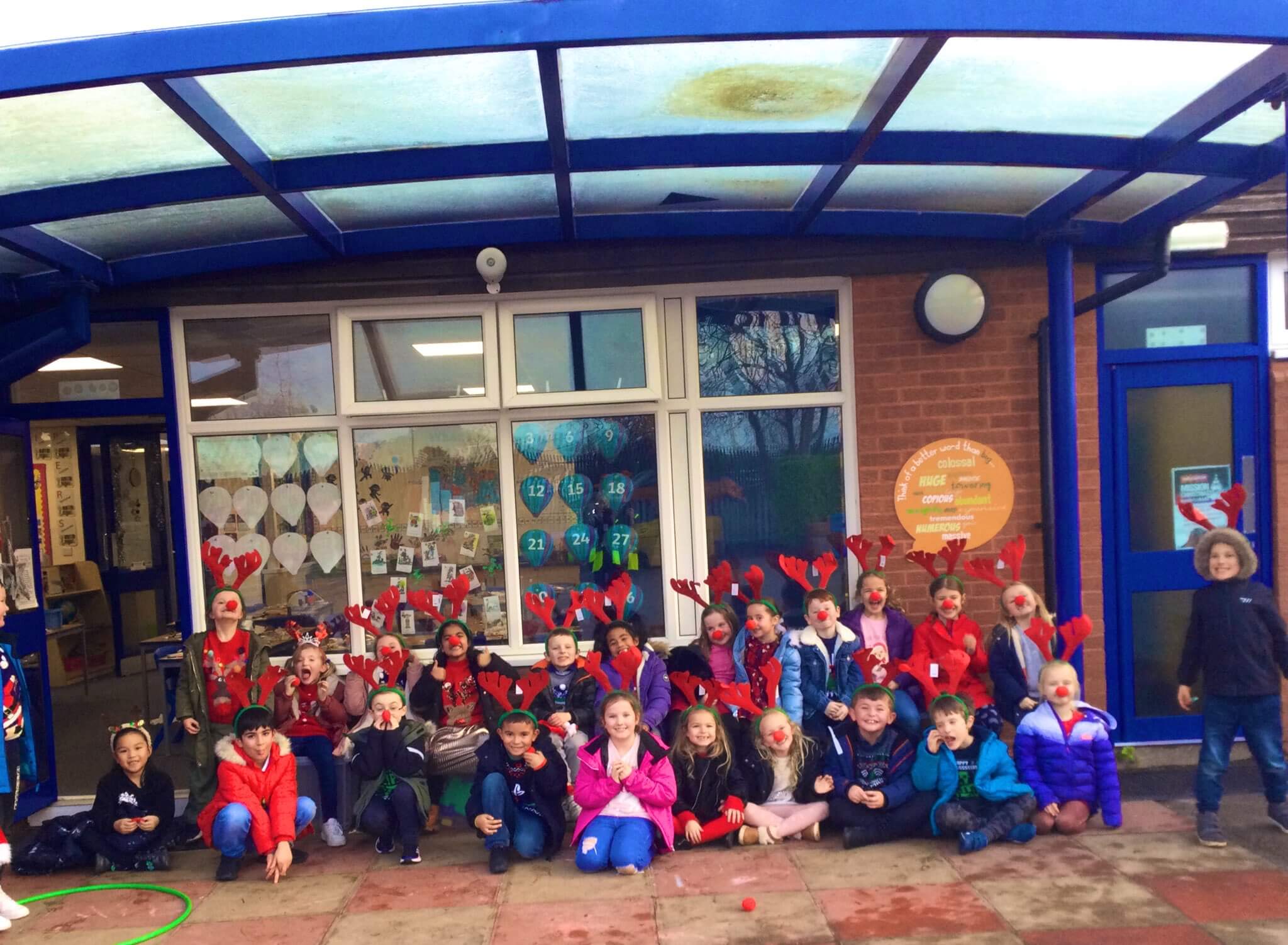 A group photo of the children who took part in the Rudolph run fundraising event. The children are wearing antlers and a red nose.