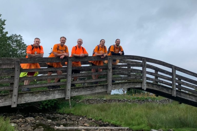 Fivee fundraiser stood on a bridge smiling. They are wearing orange hospice t-shirts and. orange tutus.