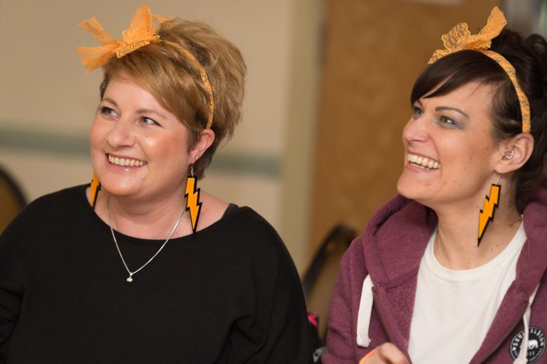 A photo of two members of the team from Victoria Medical Centre wearing orange lightening bolt earrings and orange headbands