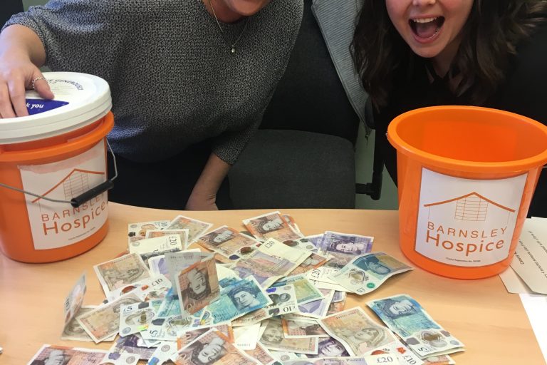 A photo of two members of the team from Victoria Medical Centre seated behind a desk full of money and two collection buckets