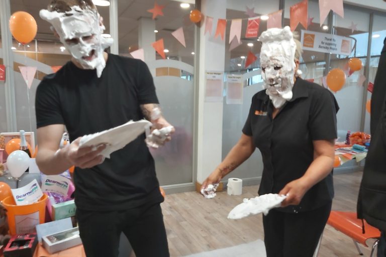 A photo of two members of the team from Webhelp with their faces covered in cream pie