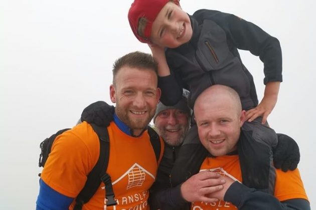 Three adult men and one child smiling. The adults are wearing orange hospice t-shirts and one is carrying the child on his shoulders.