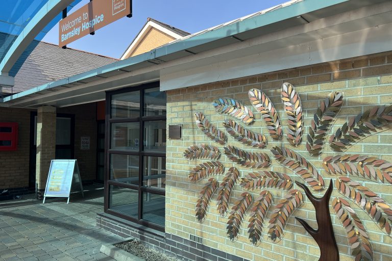 The Legacy Tree on the front of the hospice. The tree is made of a wooden trunk sculpture and individual metal leaves. The leaves are gold, silver and bronze.