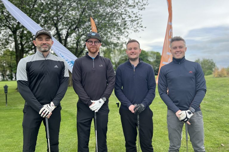 Four golfers smiling on the golf course at our golf day