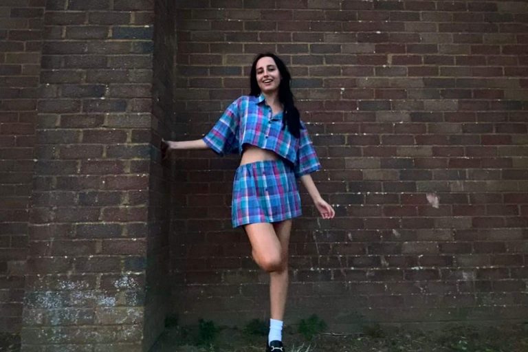 Young woman wearing transformed outfit standing against a wall