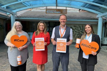 Photo of Simon Atkinson standing outside the Barnsley Hospice reception with representatives from City Taxis. The group are holding heart shaped signs saying We Care and posters in support of the hospice.