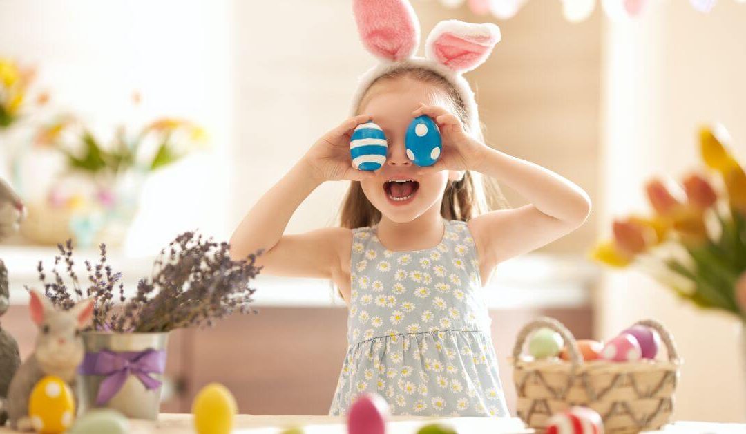 young girl with bunny ear headband holding decorated eggs in front of her eyes