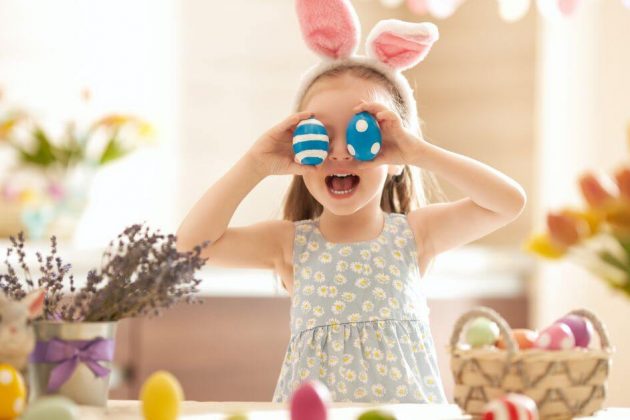 young girl with bunny ear headband holding decorated eggs in front of her eyes